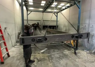Large fabricated steel frame during surface preparation inside the Salt City Metal Coatings shop.