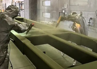 A technician applying powder to a large green fabricated frame inside the Salt City coating booth.